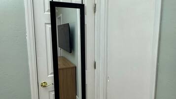 A white door with a black-framed mirror, a light green wall, and a wooden floor.