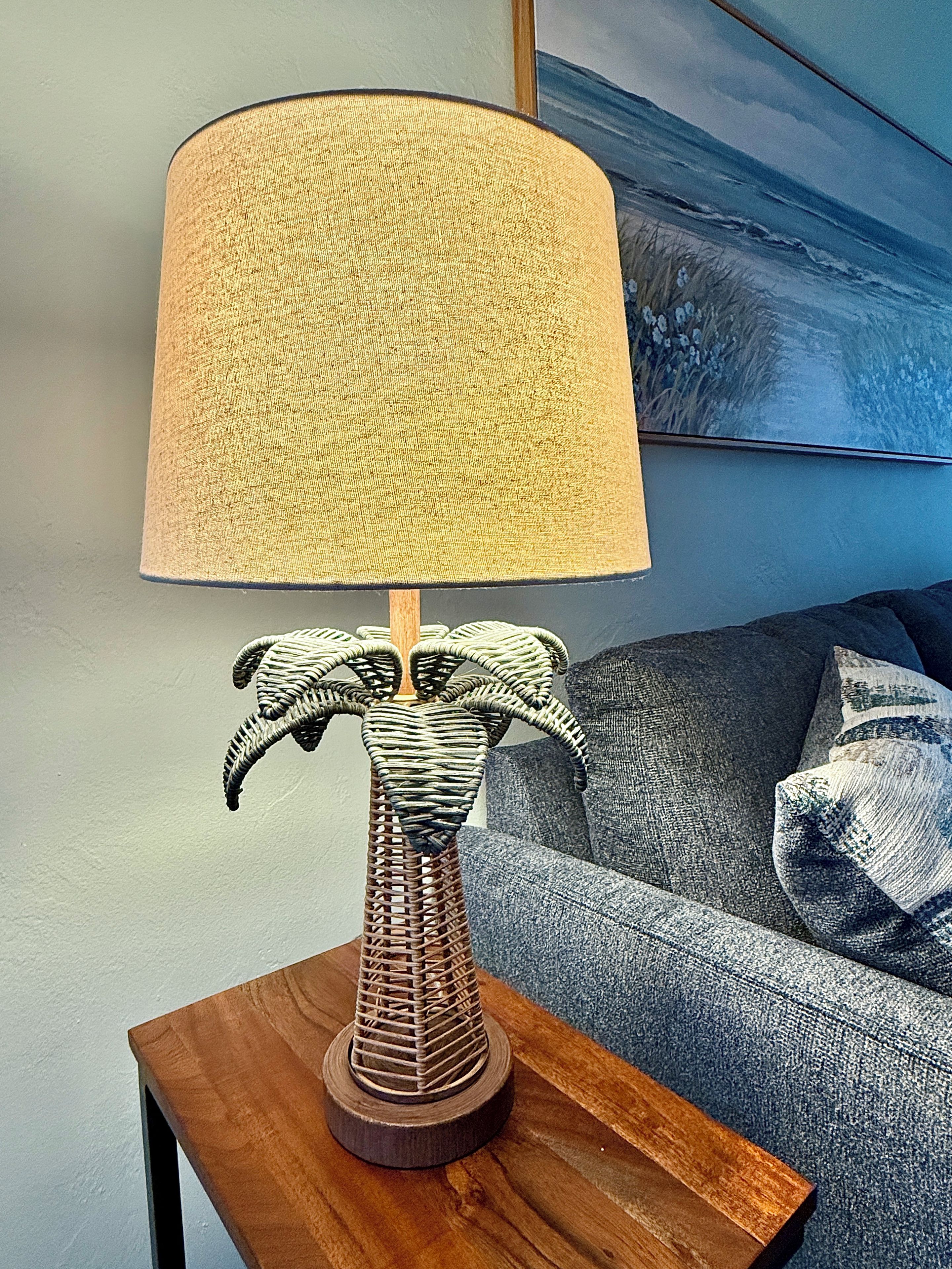 Une lampe avec un abat-jour texturé et un pied en osier, posée sur une table d’appoint en bois.