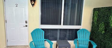 A door labeled with the number 2, two turquoise chairs, a small table, and a window with curtains.