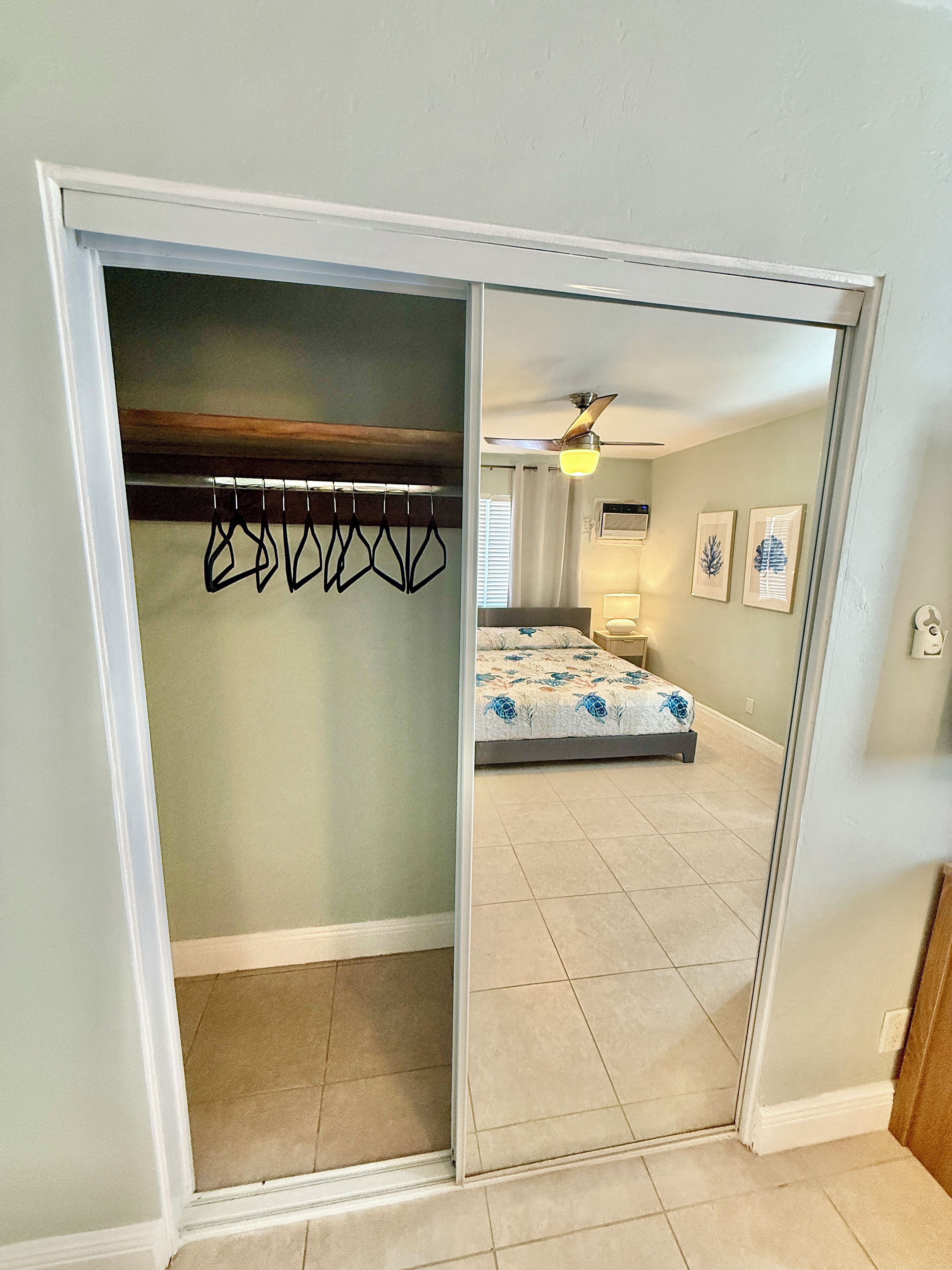 A room with a bed, a ceiling fan, and a closet with a coat rack.
