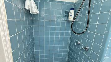 Ducha con azulejos azules, suelo a cuadros y cabezal de ducha manual.