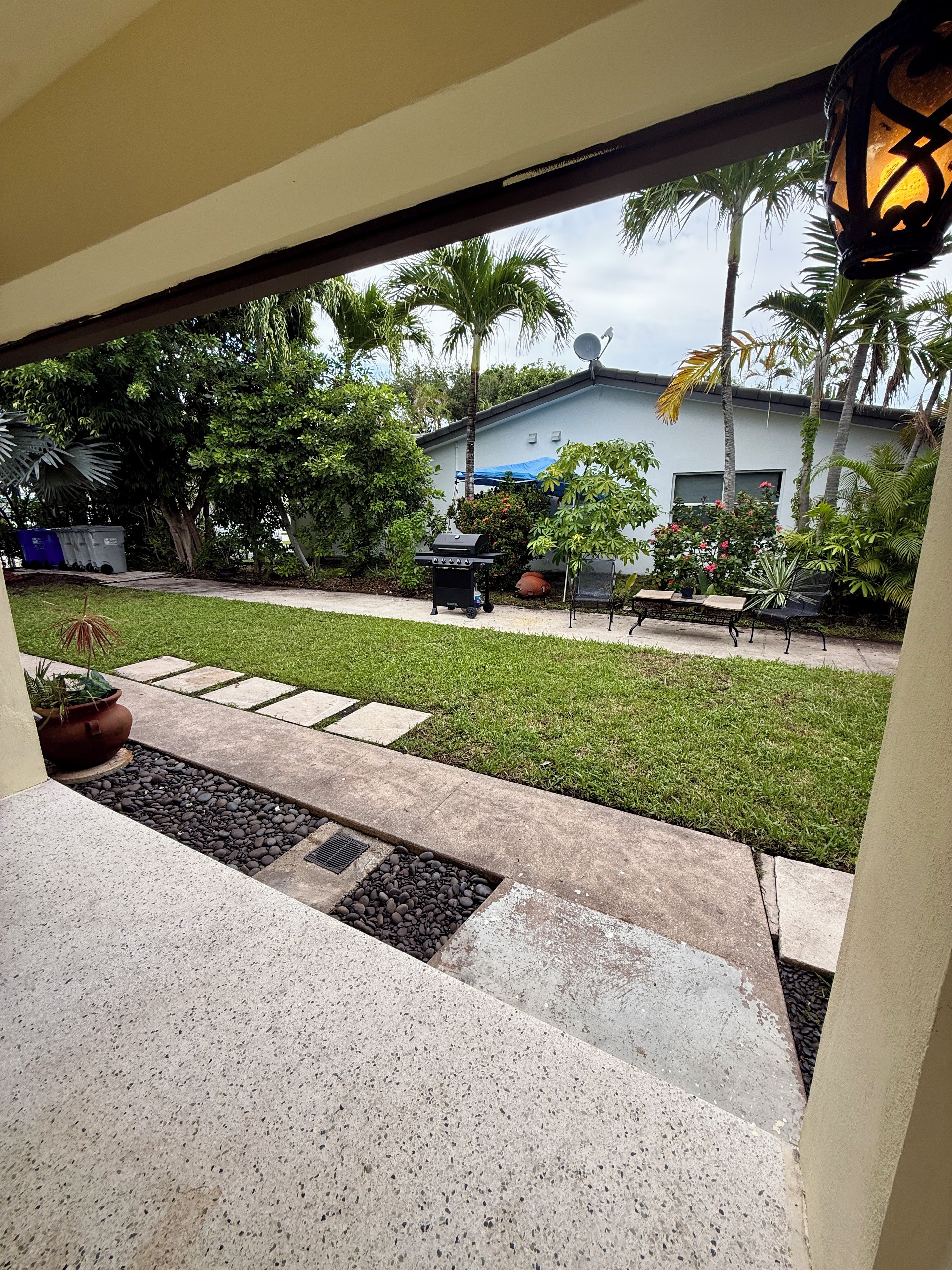 A patio with a grill, outdoor furniture, and a view of a house with palm trees.