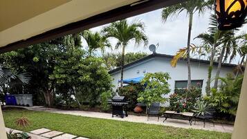 A patio with a grill, outdoor furniture, and a view of a house with palm trees.