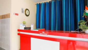 Un mostrador de recepción con un reloj, un cartel que dice 'OYO GUEST OF HONOUR' y un fondo de cortina azul.