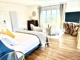 A hotel room with a large bed, a TV, a desk, and a view of the outdoors.