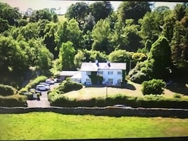 A large white building surrounded by lush greenery and a parking area.