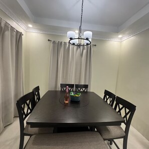 A dining room with a dark wooden table, six chairs, a chandelier, and a bottle of champagne on the table. - Trenz De Luxe (May Pen)