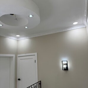 A hallway with white walls, a ceiling with recessed lighting, and a door with a black handle. - Trenz De Luxe (May Pen)