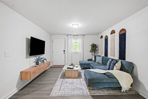 Una sala de estar moderna con un televisor de pantalla plana, un sofá azul, un aparador de madera y una alfombra estampada.