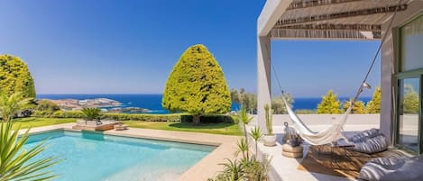Un área de piscina moderna al aire libre con vista despejada al océano, una hamaca y un jardín bien cuidado.