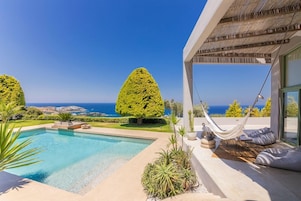 Un área de piscina moderna al aire libre con vista despejada al océano, una hamaca y un jardín bien cuidado.