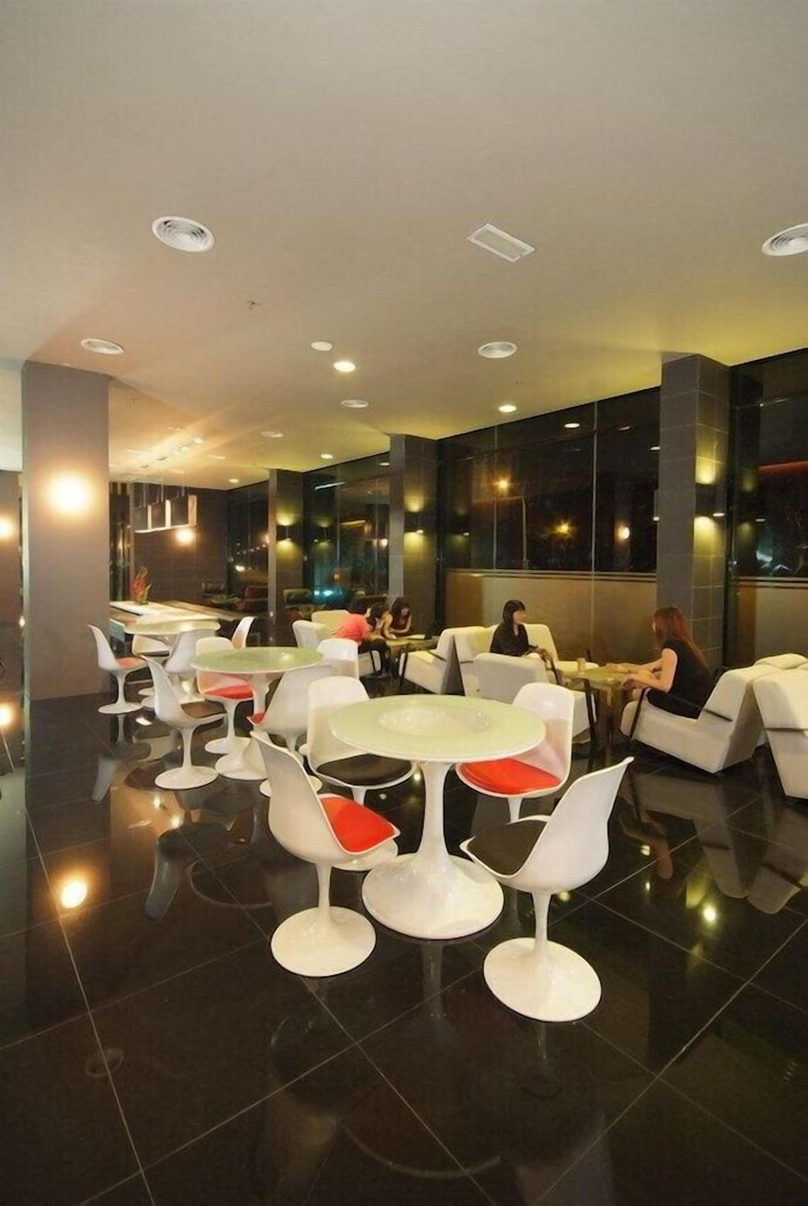 A modern restaurant interior with round tables and white chairs, featuring a polished floor and large windows.