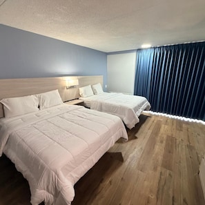 A hotel room with two beds, a wooden floor, a blue wall, and a window with curtains. - Amerihill Inn Suites Greensboro (Greensboro)