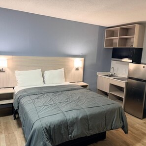 A hotel room with a bed, bedside lamps, a small desk, a refrigerator, and a TV on a shelf. - Amerihill Inn Suites Greensboro (Greensboro)