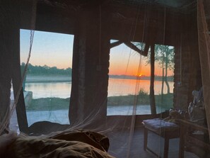 Una habitación con cama, una silla y vistas a un atardecer sobre el agua.