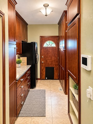 A narrow kitchen with wooden cabinets, a black refrigerator, a door with a window, and a thermostat on the wall.