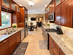A kitchen with wooden cabinets, granite countertops, stainless steel appliances, and a dining area with a chandelier. - Spacious 7-bedroom home with heated pool and Jaccuzzi (Oklahoma City)