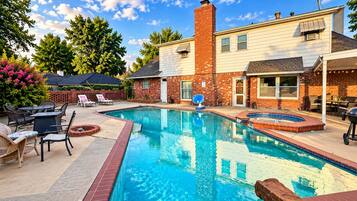 A backyard with a rectangular swimming pool, surrounded by a brick deck, and a patio area with outdoor furniture.