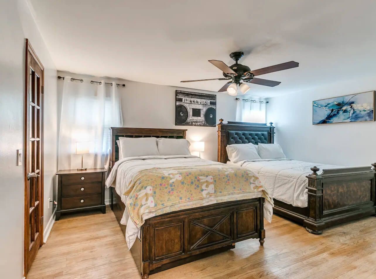 A bedroom with two wooden beds, a ceiling fan, a bedside table, and a wall-mounted radio.