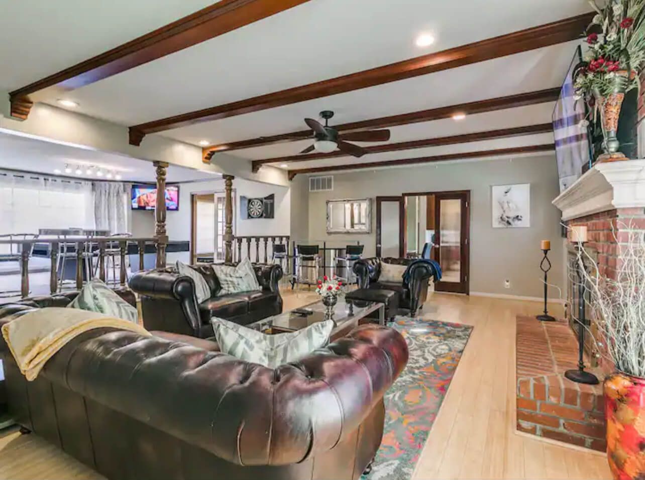 A spacious living room with a dark leather sofa, a coffee table, and a fireplace. There is a television in the background and a ceiling fan.