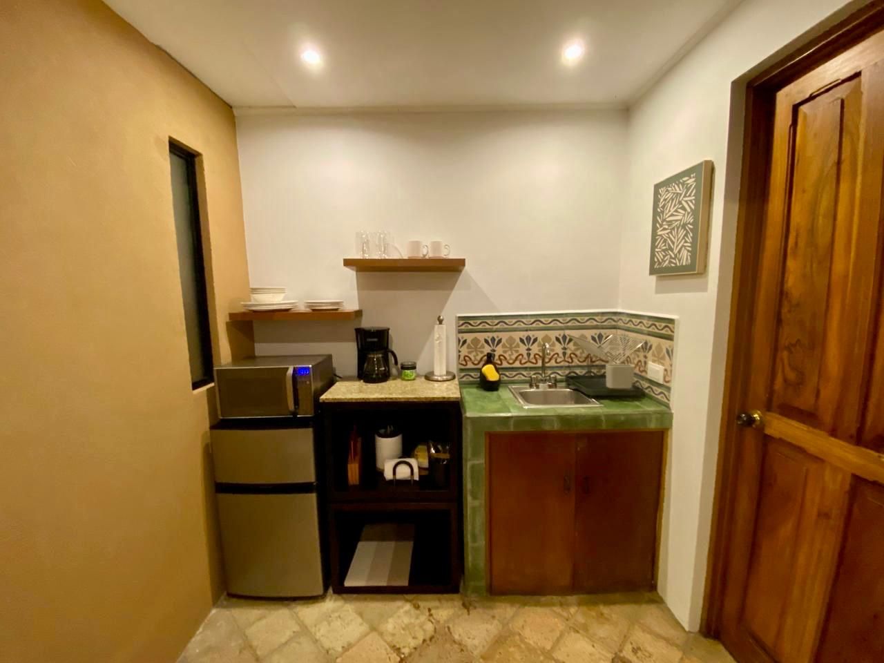 A compact kitchen with a refrigerator, a coffee maker, and a sink.