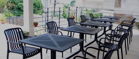 Eine Außenpatio mit mehreren Tischen und Stühlen, umgeben von einem Metallgeländer, mit Pflanzen in Töpfen im Hintergrund.