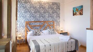 Une chambre à coucher avec un lit, une tête de lit en bois, un papier peint à motifs, une table de chevet, une lampe et un tableau accroché au mur.