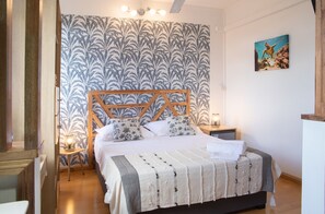 A bedroom with a bed, a wooden headboard, a patterned wallpaper, a nightstand, a lamp, and a painting on the wall. - Vrbo Property (Port Louis)