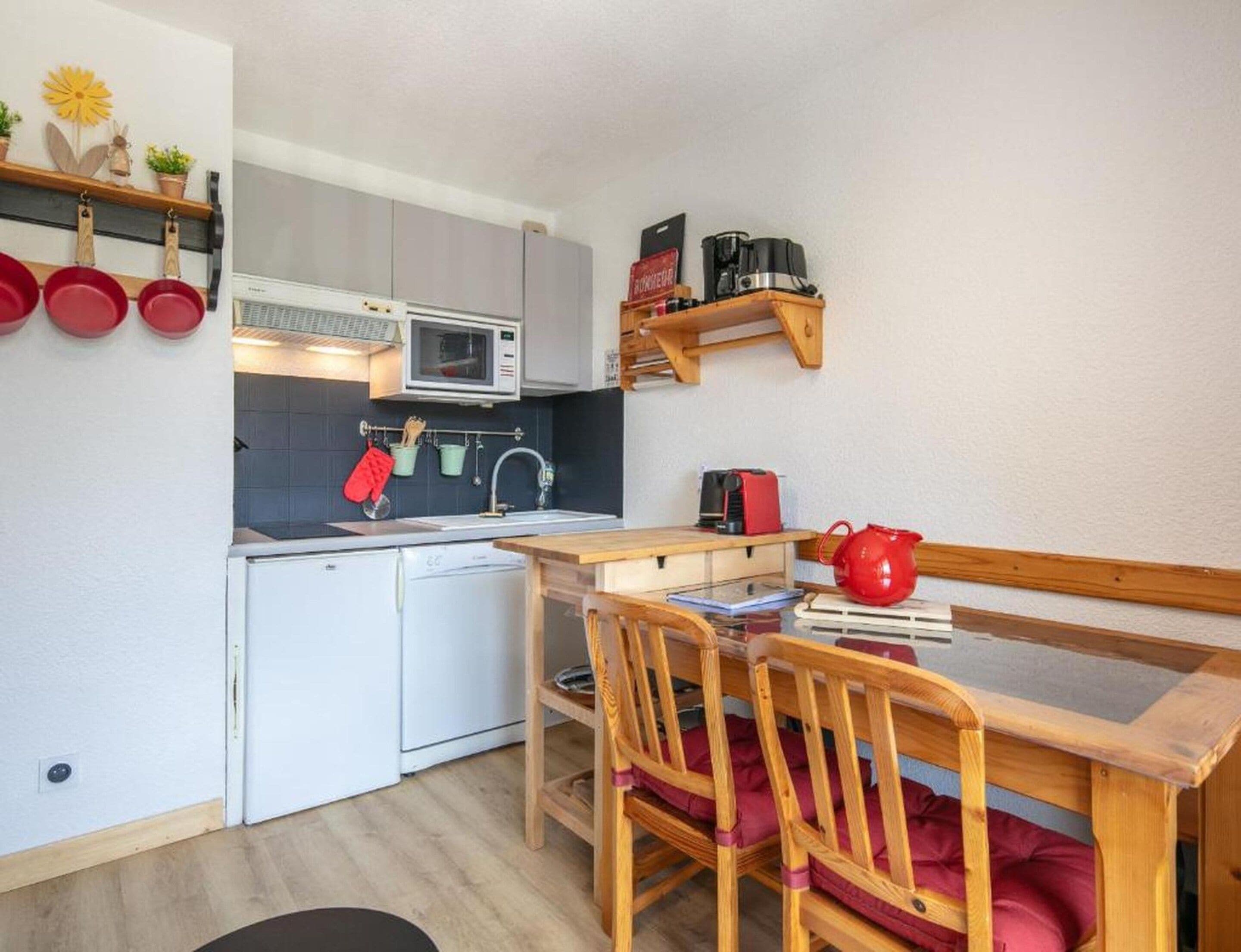 A compact kitchen with white cabinets, a microwave, a sink, and a wooden dining table with chairs.