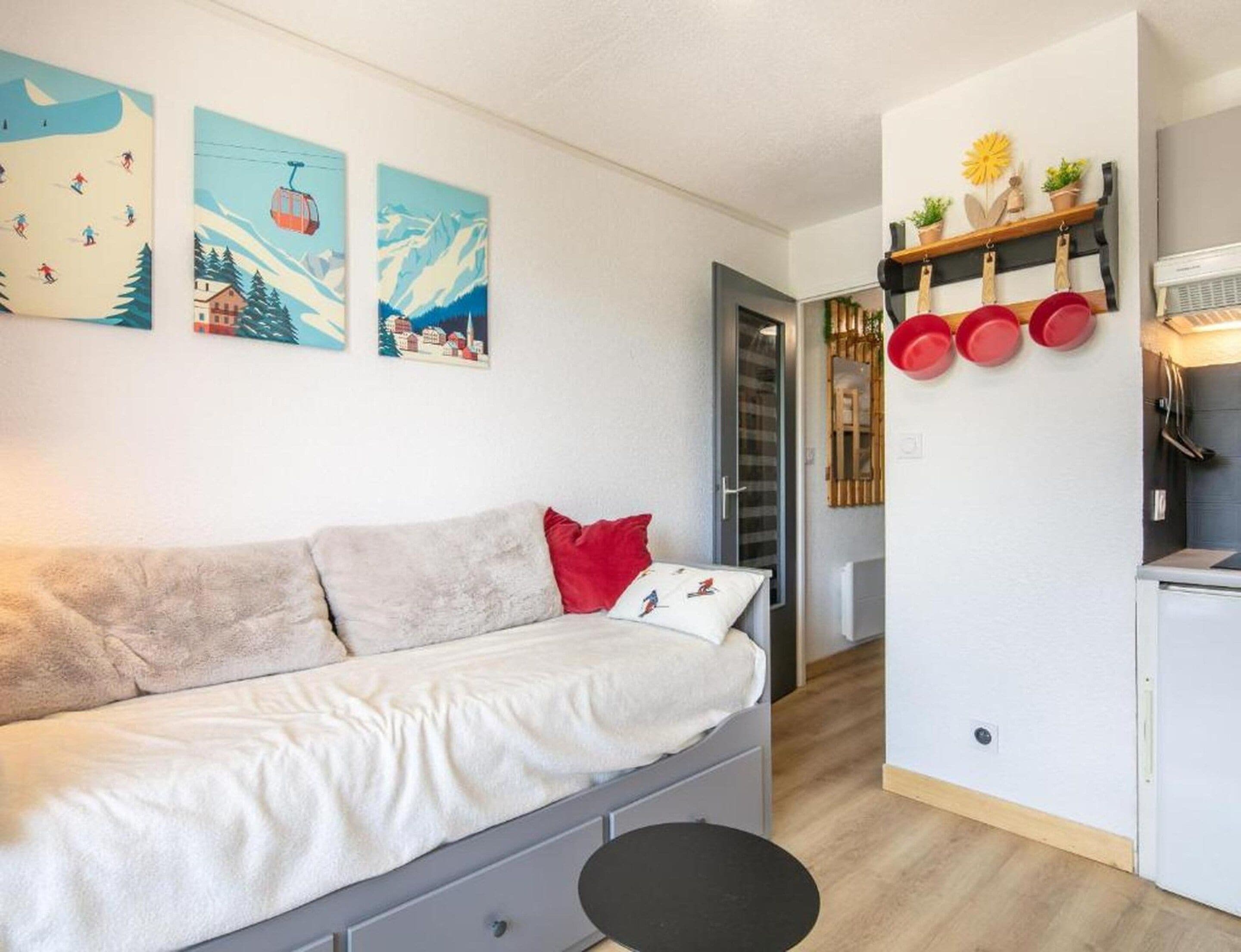 Een knus woongedeelte met een bank, een eettafeltje en een keukenhoek, inclusief pannen die aan de muur hangen.