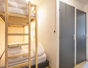 A bunk bed with a wooden frame and white bedding, a grey door, and a light switch on the wall. - Alpine Ski Apartment in Tignes for 4 (Saint-Sorlin-d'Arves)