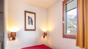 Habitación con cama, dos lámparas de pared, un cuadro enmarco y una ventana con vista a un paisaje montañoso.