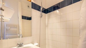 Un baño con lavamanos blanco, un espejo, ducha y toallero.