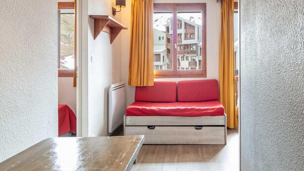 Habitación compacta con cama, mesa, lámpara de pared y ventana con cortinas.