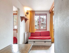 Ein gemütlicher Raum mit Bett, Tisch, Wandlampe und einem Fenster mit Vorhängen.