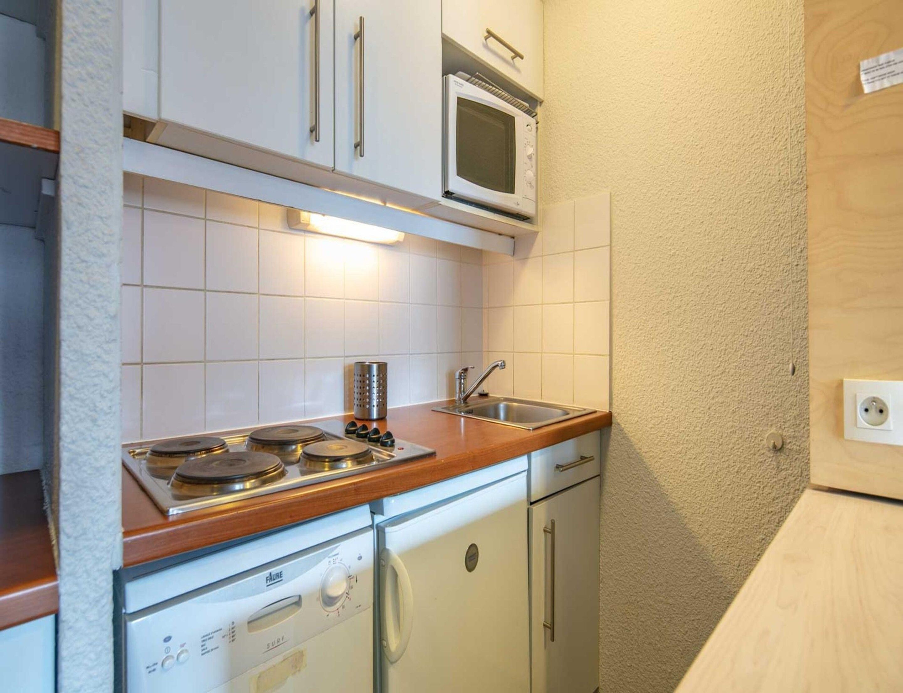 A compact kitchen with white cabinets, a microwave, a stove, and a dishwasher.