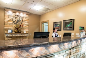 A reception desk with a stone wall, a large 'P' logo, and framed pictures on the wall. - Podollan Rez-idence Fort Mcmurray (Fort McMurray)