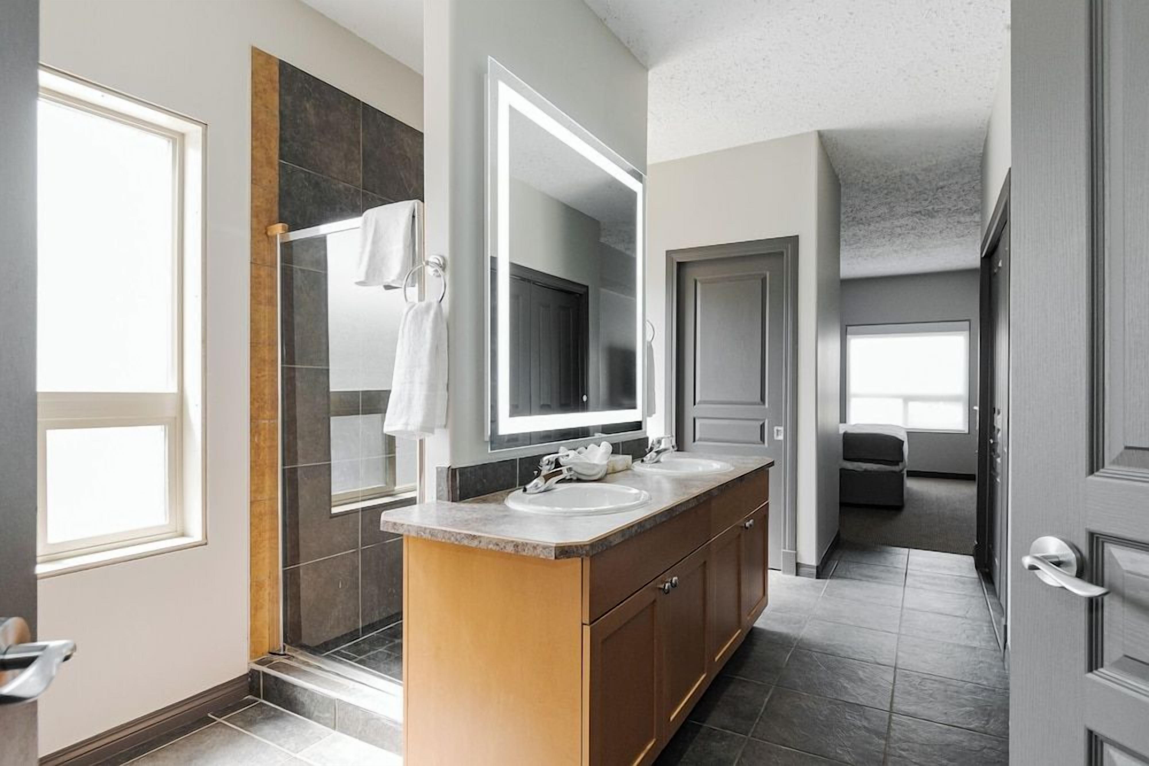 A modern bathroom with a large mirror, two sinks, and a shower.
