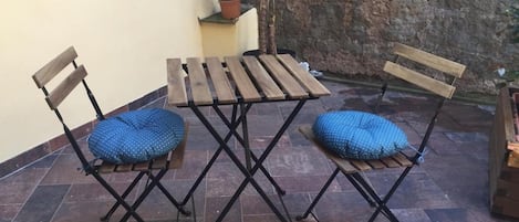 A patio with a wooden table and two chairs, a small potted plant, and a stone wall.