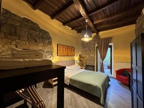 A bedroom with a stone wall, a bed with a green blanket, a wooden table with towels, a red chair, and a hanging light fixture. - B and B Al Cardinale (Viterbo)