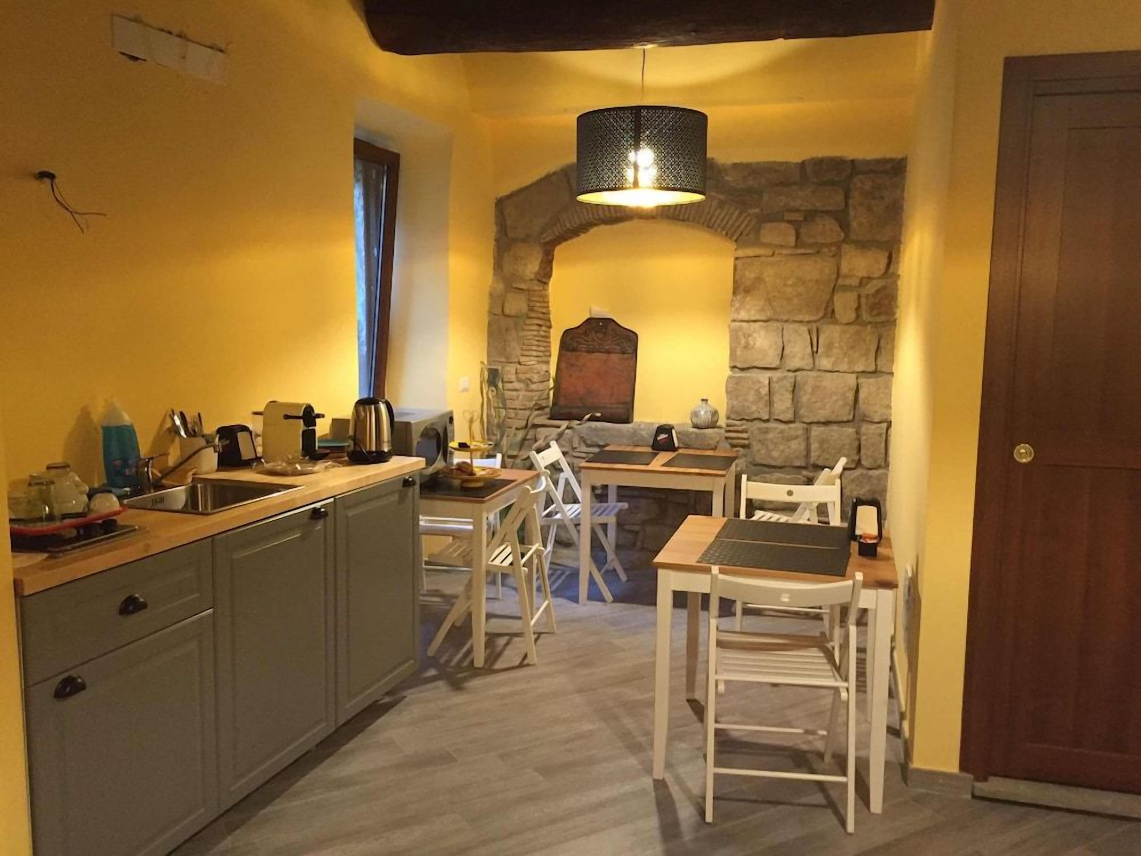 Uma cozinha compacta com um arco de pedra, porta de madeira e área de refeições com cadeiras brancas.