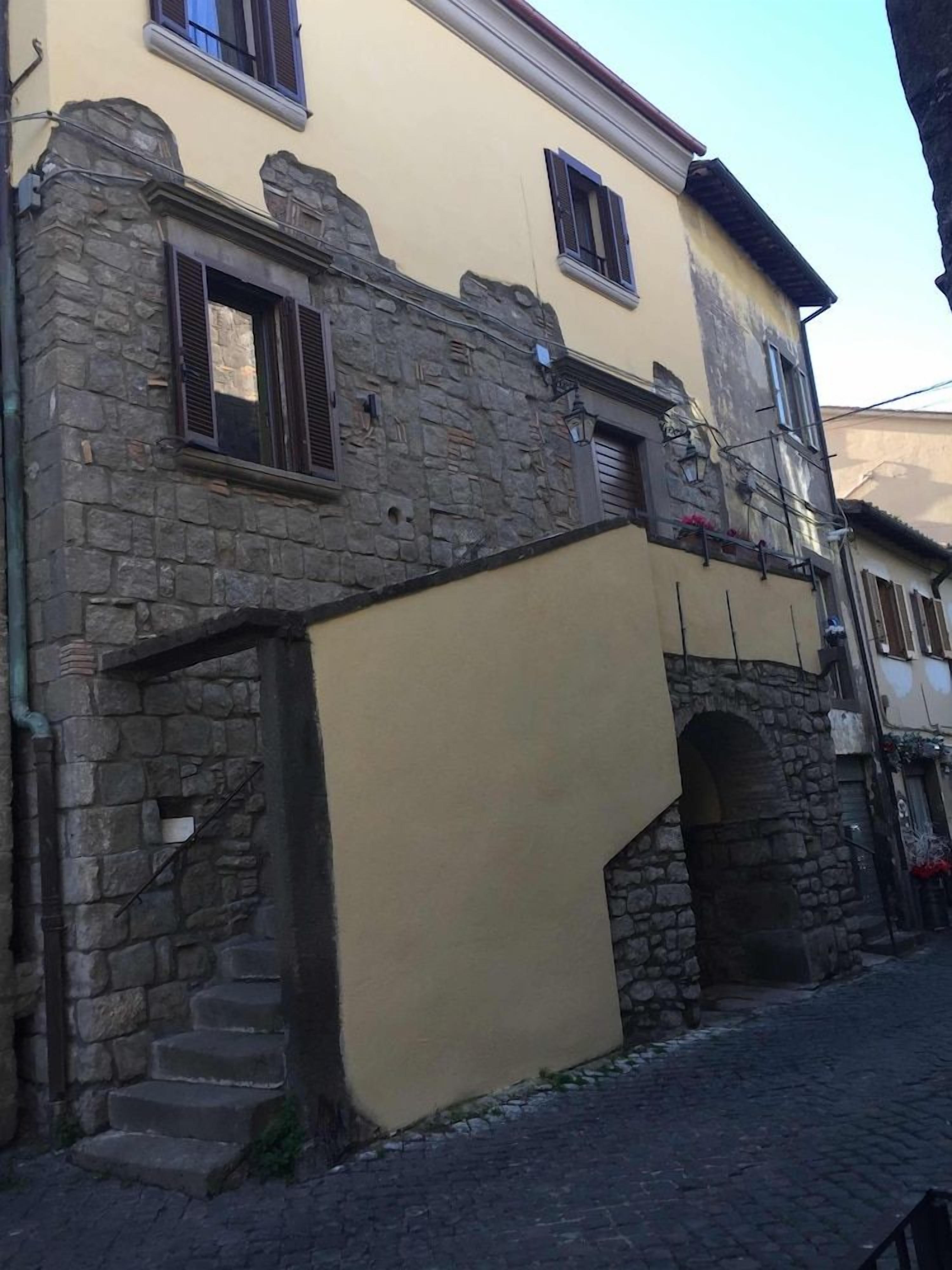Um edifício com fachada de pedra, seção superior amarela e escadaria visível que leva a uma entrada.