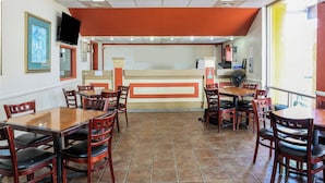 A restaurant interior with wooden tables and chairs, a counter with a menu, and a framed picture on the wall. - Magnuson Hotel Opelika (Opelika)