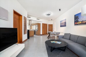 Ein modernes Wohnzimmer mit Flachbildfernseher, grauem Sofa, Couchtisch und Essbereich mit Glastisch und grauen Stühlen.