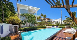 A modern hotel with a swimming pool, palm trees, and a clear blue sky. - Ultravioleta B102: Direct Beach & Pool Walk-out Oceanfront One-Bedroom apartment (Cabarete)