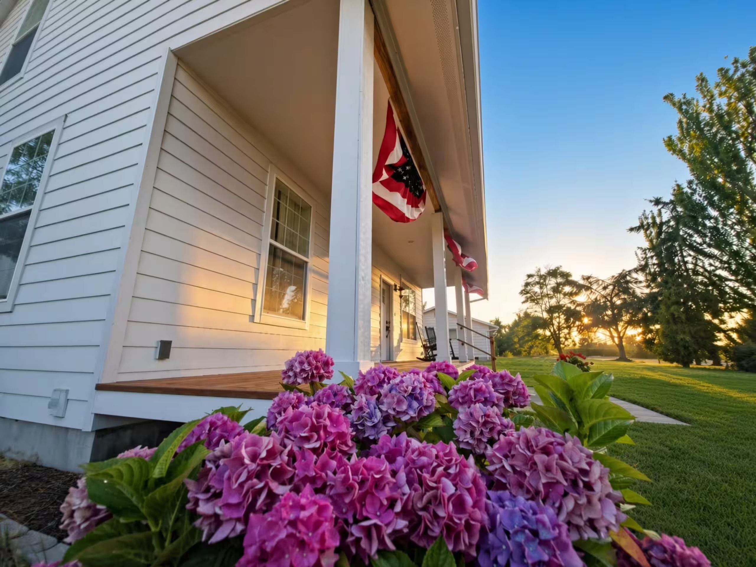 Uma casa com varanda, bandeira americana e flores de hortênsia.