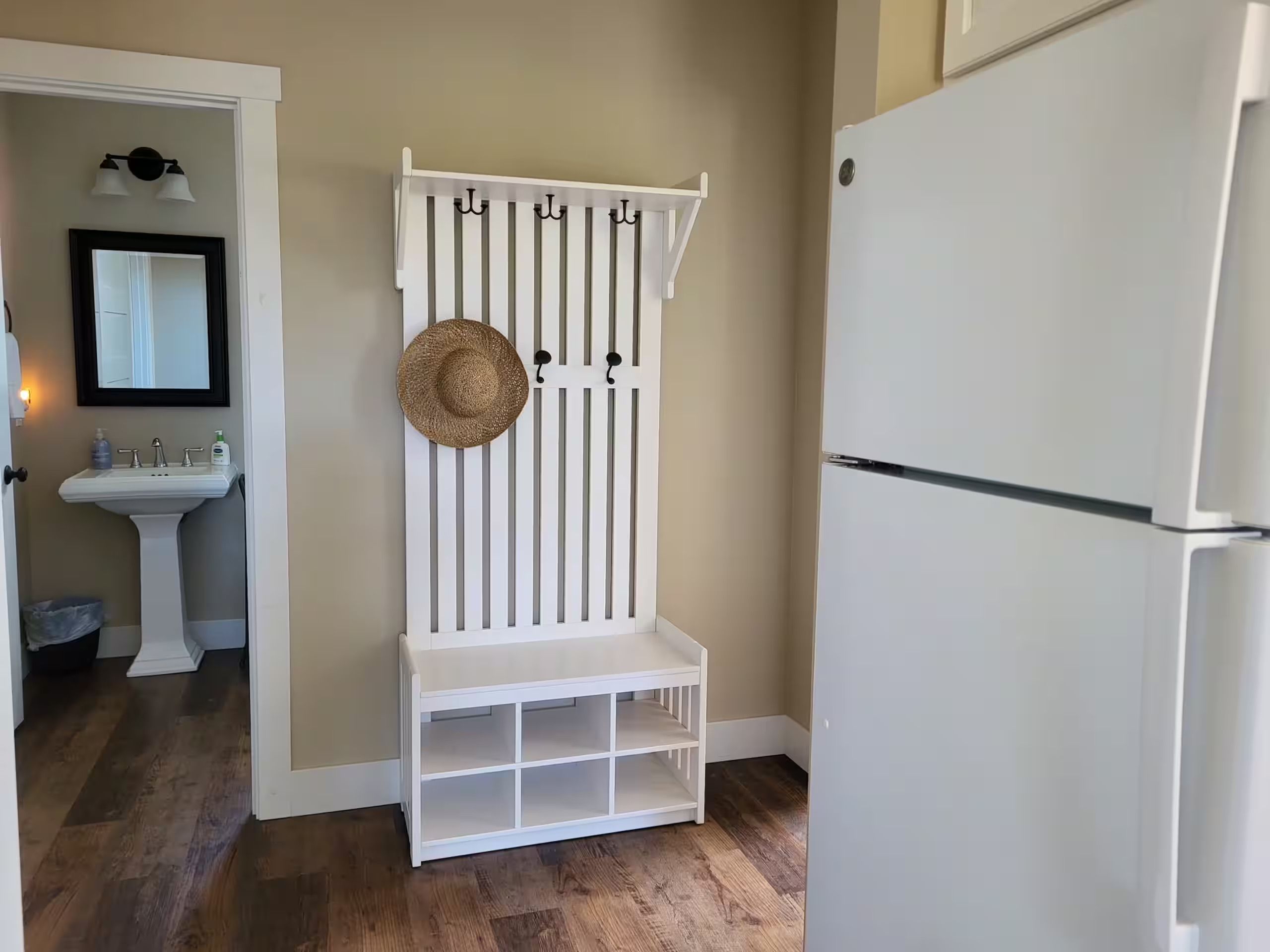 A kitchen with a white refrigerator, a white bench with storage, a sink, and a mirror.