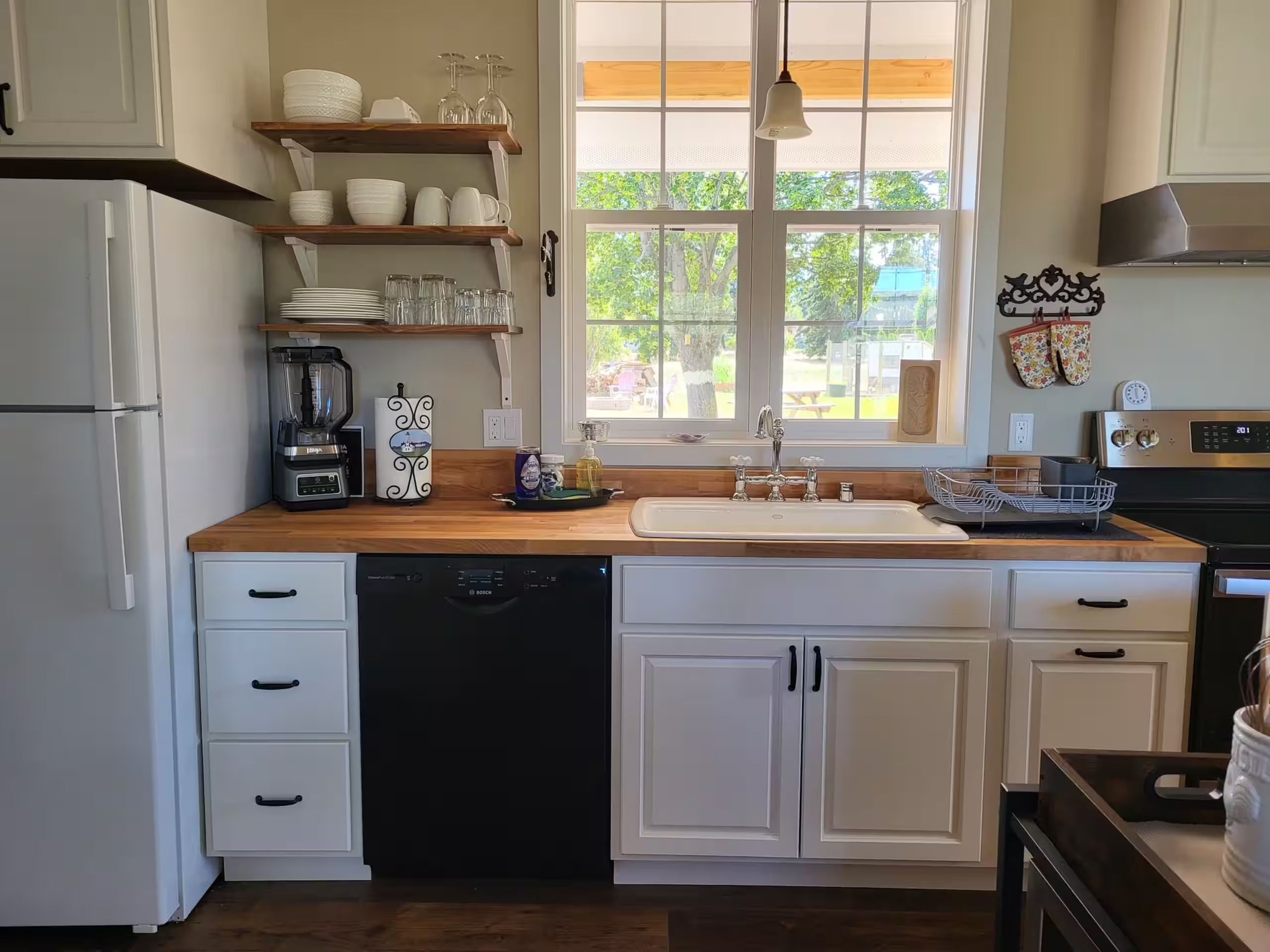 A kitchen with white cabinets, a dishwasher, a sink, and a window with a view of greenery outside.