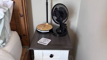 Ein Nachttisch mit Lampe, Ventilator und kabellosem Ladegerät.