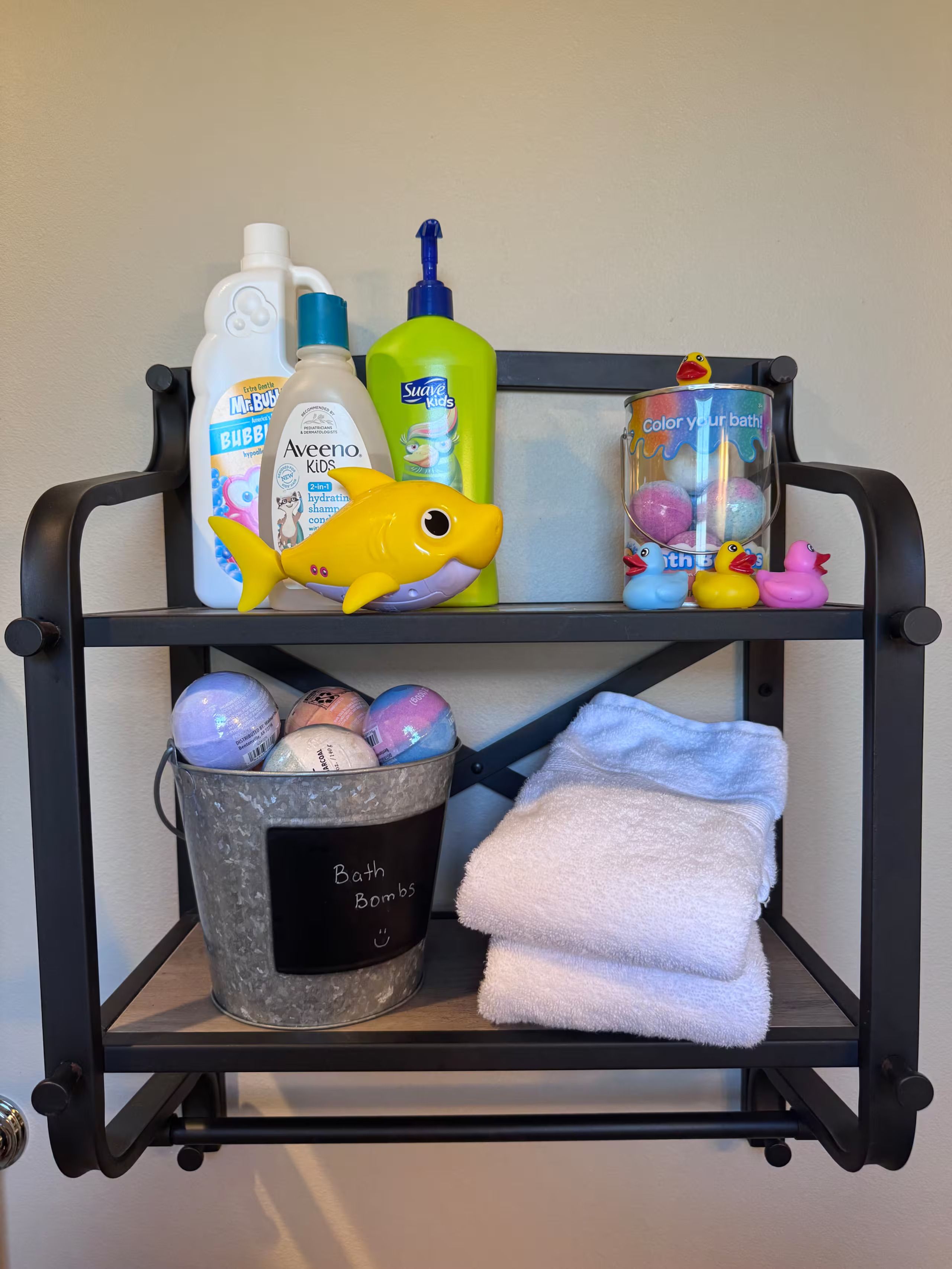 Une étagère en métal noir sur laquelle sont posés des articles de toilette, des bombes de bain et un jouet en peluche.